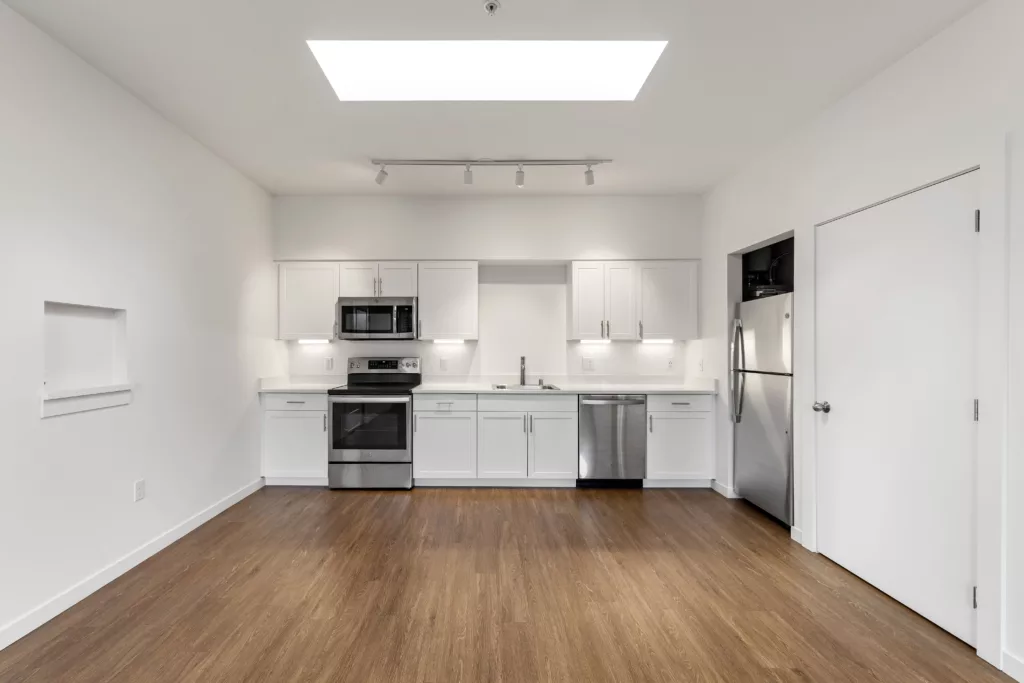 Modern kitchen with white cabinets, stainless steel appliances, wood flooring, and a skylight.