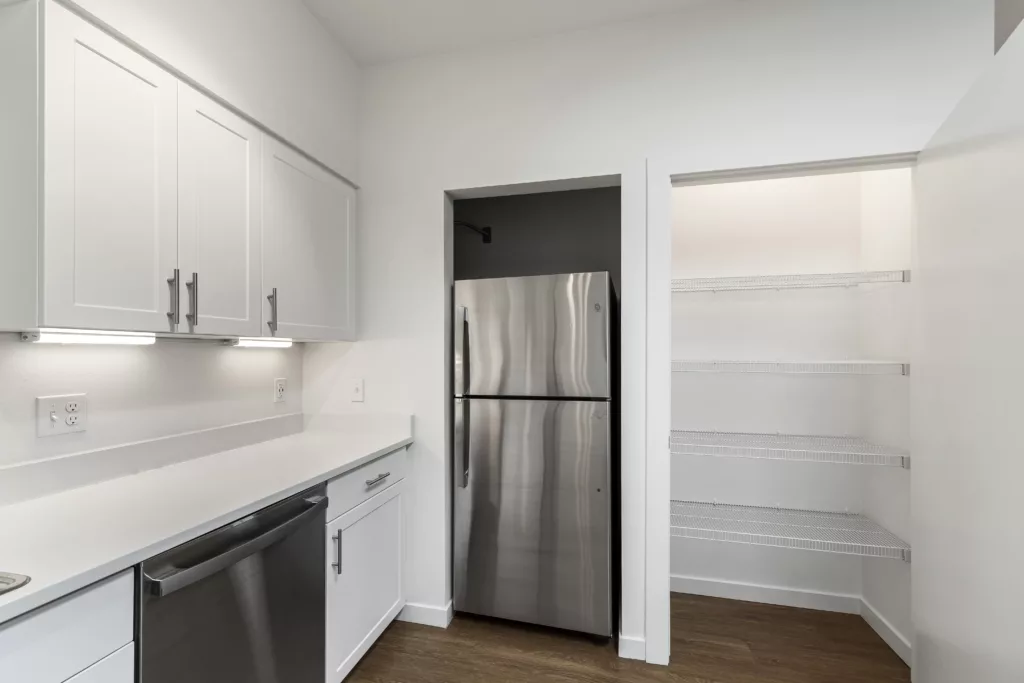 A modern kitchen with white cabinets, stainless steel appliances, and an open pantry with wire shelves.