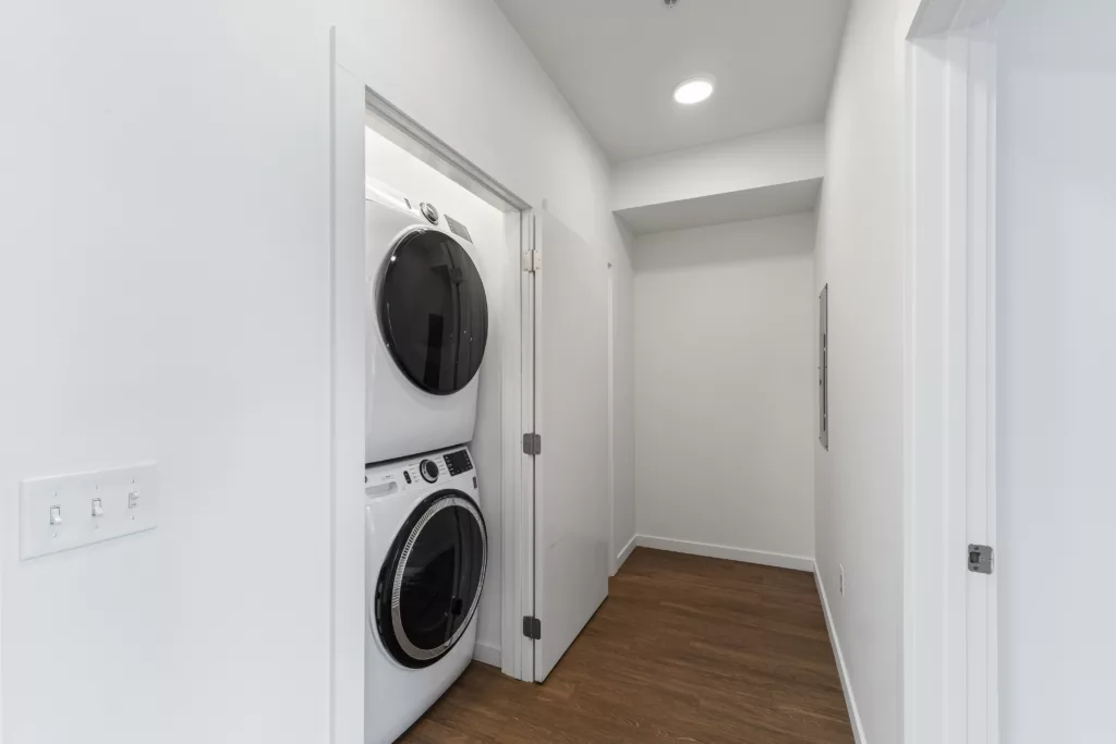 A small laundry room with a white stackable washer and dryer on a wooden floor.