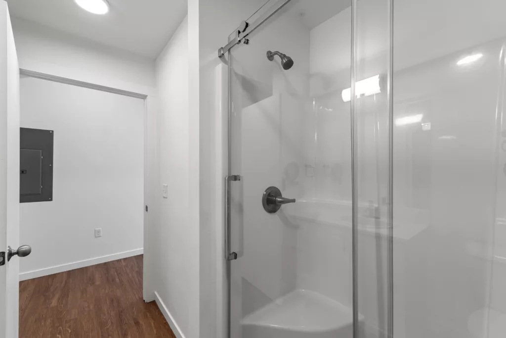 A modern bathroom with a glass-enclosed shower and hardwood flooring.